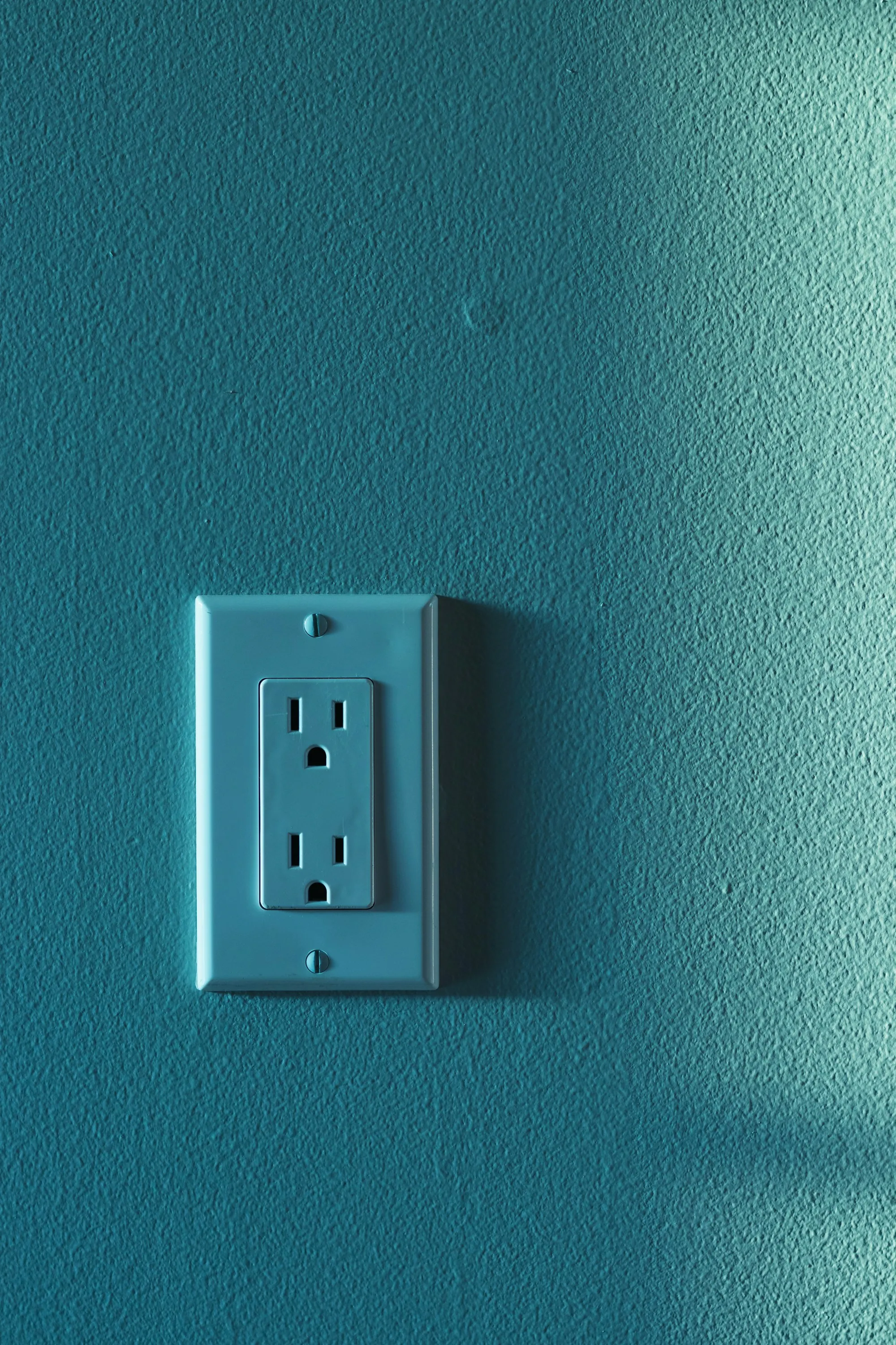 Single new electrical outlet mounted on a painted teal wall
