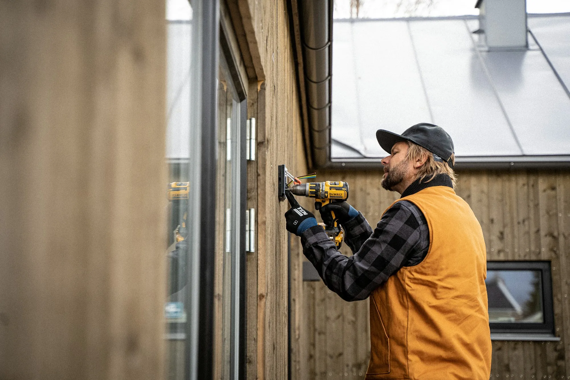 Electrician drilling a wall bracket for new wiring in a wood-clad house